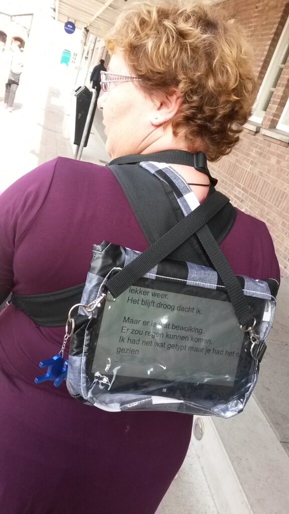Gea in paars shirt draagt op haar rug een hoes met daarin een tablet met tolktekst
